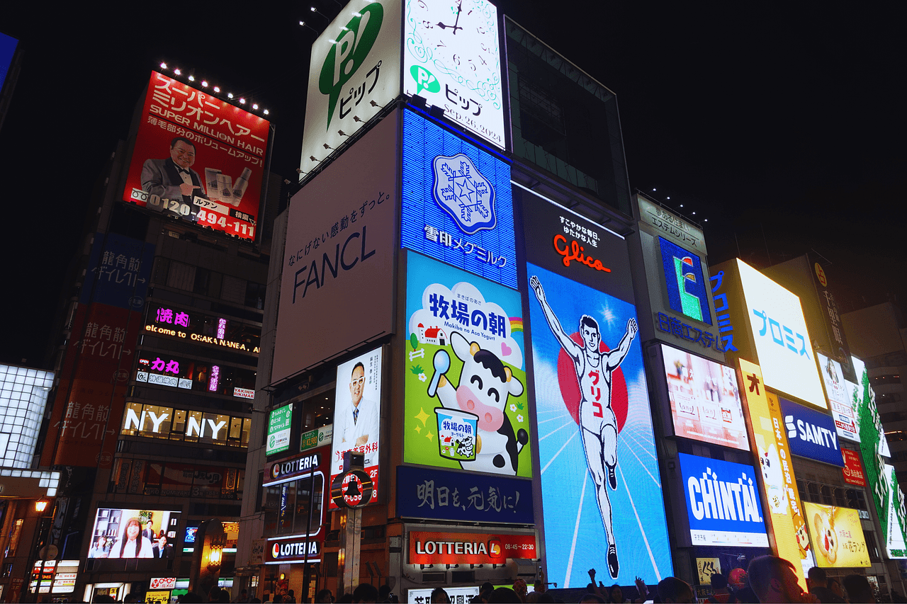 Night view of Dotonbori in Osaka, Japan, featuring the iconic Glico Running Man billboard and colorful neon signs.