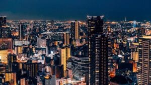 Night view of Osaka city skyline with brightly lit skyscrapers and buildings glowing under a dark blue sky, showcasing the urban energy of Japan.