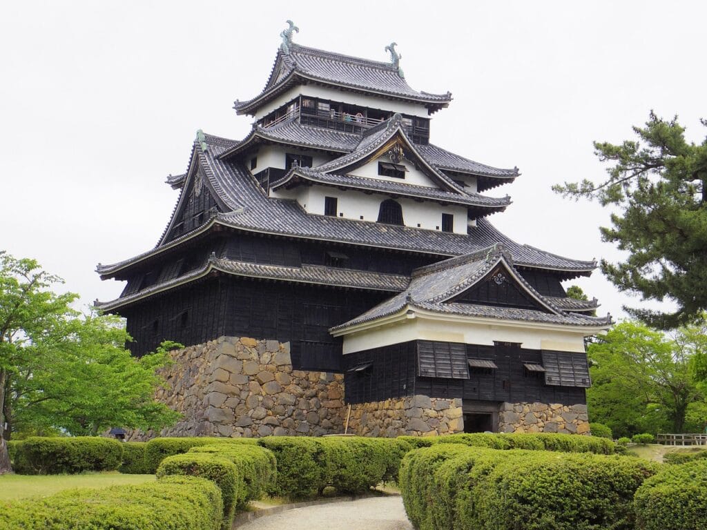 Historic Japanese castle with black wooden walls and stone base surrounded by manicured gardens
