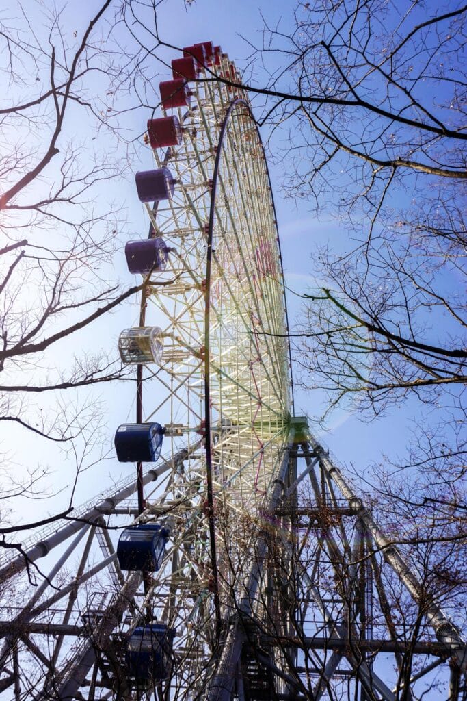 osaka city japan vertical image of tempozan giant ferris wheel and winter trees branch on bright blue sky with sun and lens flare background at tempozan harbor village osaka japan