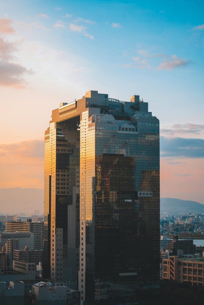 A striking modern skyscraper reflecting sunset hues against a vibrant cityscape.