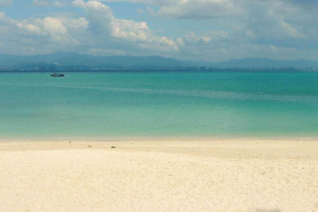 Quiet tropical beach with turquoise waters and distant mountains under a cloudy sky