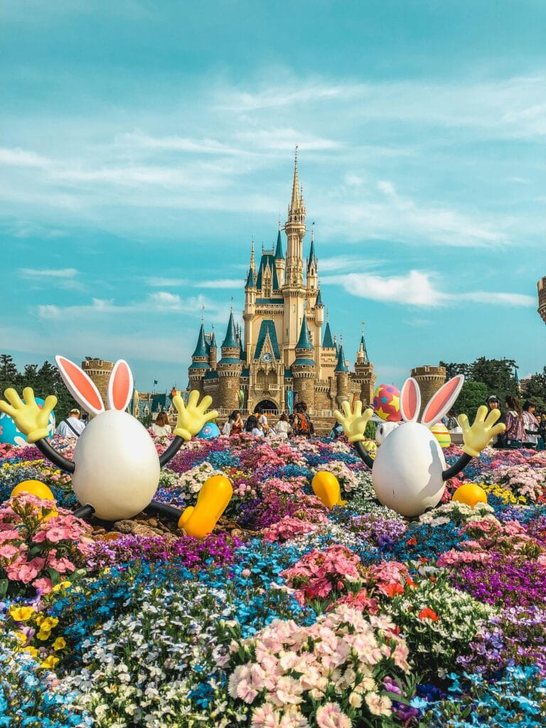 Vibrant flowers and playful decorations adorn the iconic Tokyo Disneyland Castle in a festive springtime setting.