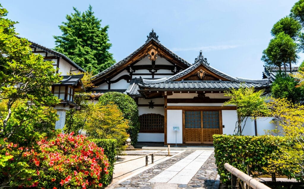 A serene traditional Japanese temple surrounded by lush gardens under clear daylight.