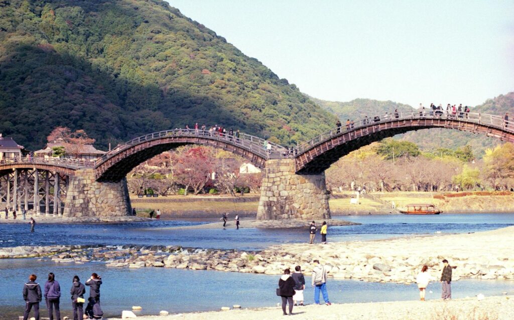 Scenic view of Kintai Bridge in Iwakuni, Japan with tourists enjoying the picturesque landscape.